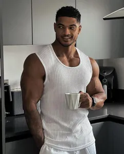 Muscular man wearing a white ribbed fitness tank top in a modern kitchen setting.