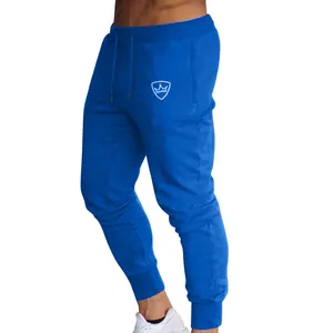 Close-up of men's royal blue slim fit joggers with white shield logo and drawstring.