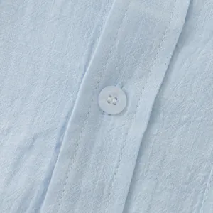 Close-up detail of light blue linen shirt showing fabric texture and button sewing quality