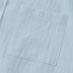 Macro detail of a light blue linen shirt's front pocket showing fabric texture