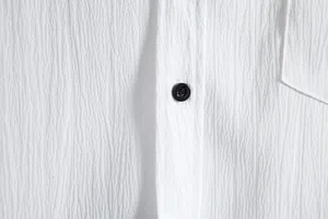 Close-up detail of white textured fabric and black button on a men's shirt.