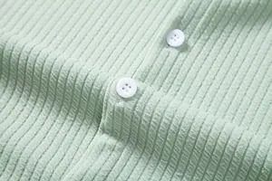 Macro detail of mint green ribbed shirt fabric showing white buttons and texture