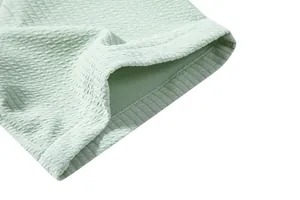 Close-up view of light green textured fabric showing waffle pattern and precise hem stitching