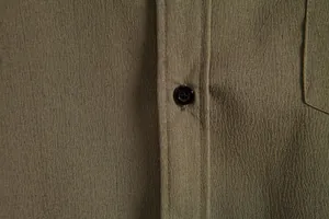 Close-up detail of an olive green casual shirt showing fine fabric texture and button placket