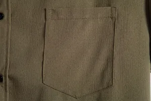 Macro view of a chest pocket detail on an olive green textured casual shirt for men.
