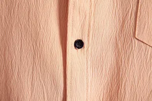 Macro view of textured peach fabric with a dark blue button on men's casual shirt