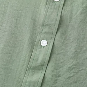 Detailopname van groene linnen stoftextuur en witte knoop op een heren zomeroverhemd