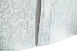 Close-up detail of textured crinkle fabric and fine stitching on a white men's shirt.