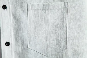 Macro view of textured white shirt fabric showing chest pocket and black buttons