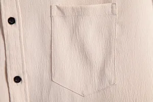 Macro view showing the crinkle texture and chest pocket of a beige men's casual shirt