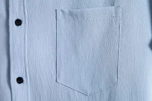 Close-up detail showing the pocket and fabric texture of a light blue men's casual shirt