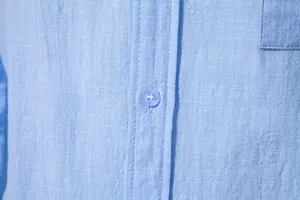 Detailed macro shot of light blue cotton linen shirt fabric texture and blue button