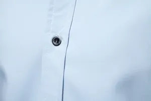Close-up detail of the black button and white stitching on a light blue men's shirt