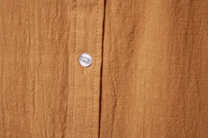 Macro detail of ochre cotton linen shirt featuring fabric texture and white button