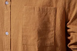 Close-up detail of cotton linen shirt pocket showing fabric texture and buttons