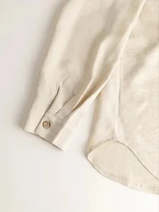 Macro detail of natural linen fabric texture on long sleeve shirt cuff and curved hem