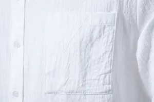 Close-up detail of a white cotton linen shirt showing the front pocket and fabric texture