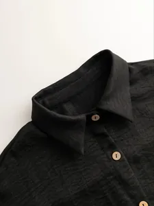 Detail view of the classic collar and natural wooden buttons on a black textured knit cardigan