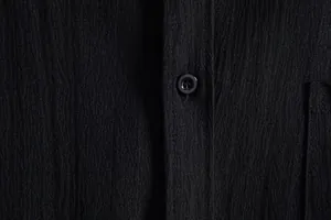 Close-up of black textured fabric and button detail on a men's casual solid shirt