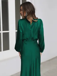 Back view of elegant emerald green satin long sleeve maxi dress showing fabric texture.