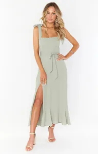 Elegant sage green sleeveless midi dress with bow straps and side slit detail.