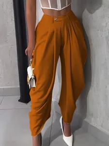 Detail of orange pleated high waist paper bag trousers with stylish wide leg silhouette.