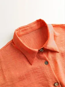 Detail view of the classic collar and dark buttons on an orange linen-texture women's shirt
