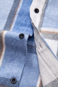 Detalle macro de una camisa de franela a cuadros azules con textura de tela y botones.