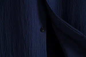 Detailed macro shot of the navy blue crinkle texture and button on this men's summer shirt