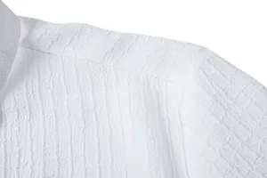 Macro detail of white textured jacquard fabric and shoulder seam on a men's shirt.