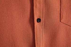 Close-up of textured rust-orange fabric on men's casual shirt with black button