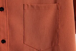 Detail macro view of rust orange men's casual shirt featuring pocket and black buttons