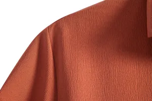 Macro detail of burnt orange men's shirt showing high-quality textured crepe fabric.