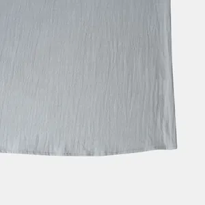 Macro detail of the curved hem and fine stitching on a grey cotton-linen shirt