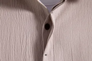 Detailed view of beige men's shirt with crinkled fabric texture and button closure