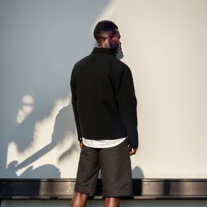 Minimalistische Rückansicht einer schwarzen Herrenjacke vor Wand mit Palmenschatten