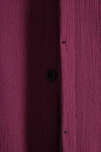 Close-up of a burgundy men's short-sleeved shirt with textured fabric and a black button