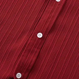 Primer plano de la tela con textura rojo oscuro y botones blancos de camisa de hombre.