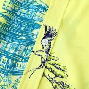Gros plan d'un tissu de chemise hawaïenne jaune avec imprimé pagode sarcelle et bouton blanc.