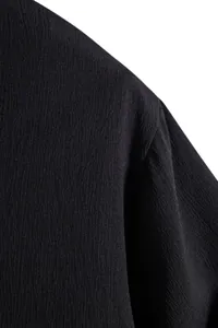 Detailed macro view of the textured black fabric and shoulder seam on men's summer shirt.