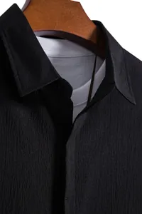 Close-up detail of black textured men's short-sleeved shirt fabric and collar.