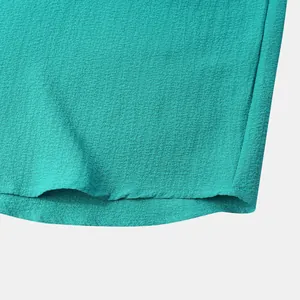 Detailed close-up of teal crepe fabric texture and hem stitching on men's summer shirt