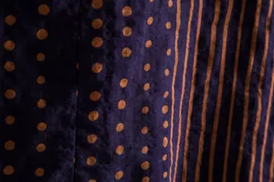 Detailed close-up view of dark purple fabric with orange polka dots and vertical stripes pattern
