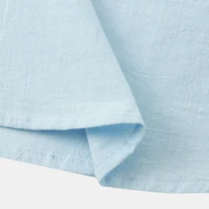 Detail view of light blue breathable cotton linen shirt showing fabric texture and hem.