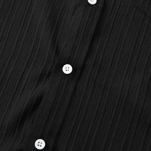 Primer plano de la tela negra texturizada y botones blancos en una camisa de hombre.