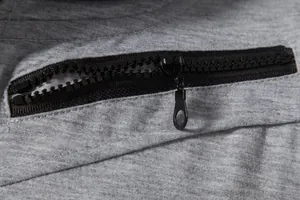 Gros plan sur la fermeture éclair noire en résine d'un gilet de sport gris pour homme.