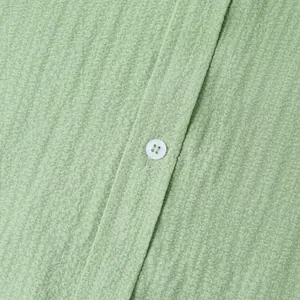 Macro view of sage green textured seersucker fabric and white button detail on summer shirt