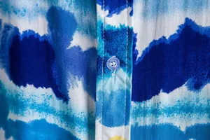 Macro detail of blue tie-dye printed casual shirt fabric showing button and stitching.