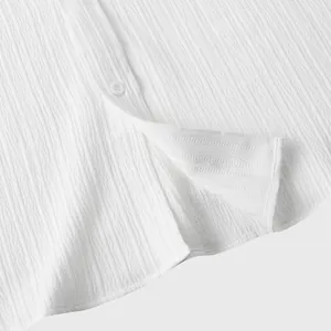Detalle de cerca del tejido texturizado blanco y el botón de una camisa de verano para hombre