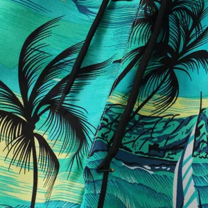 Close-up detail of teal tropical palm tree print beach shorts with black drawstring